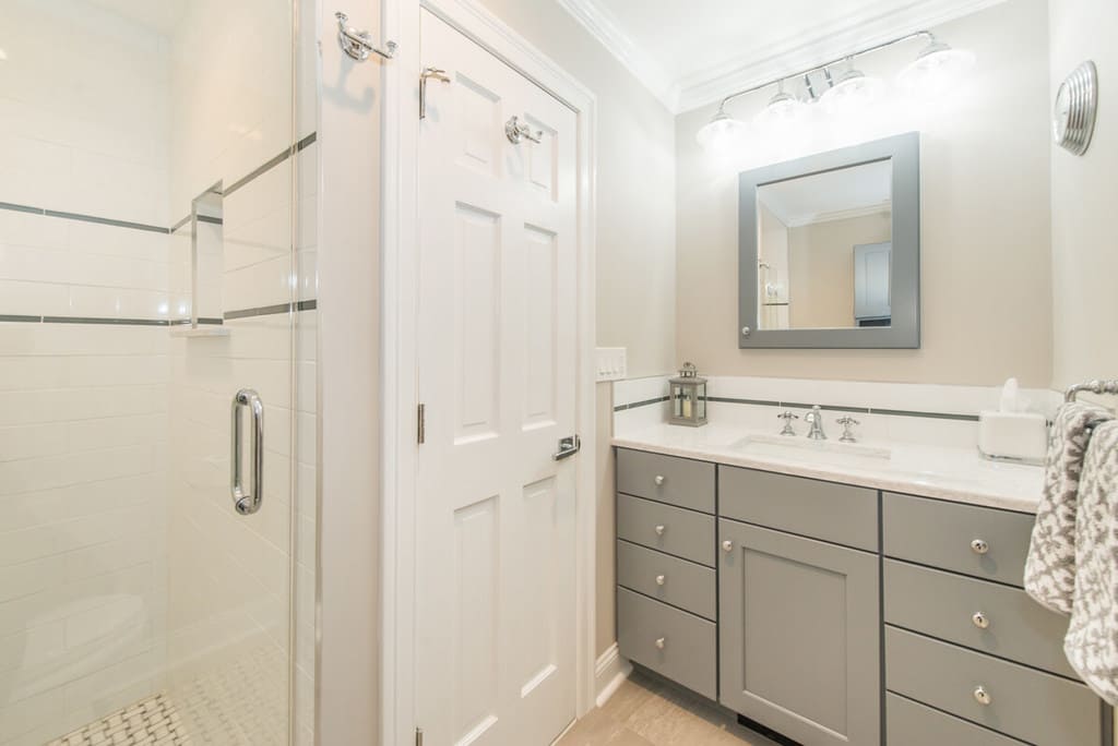 Grey and white hall bathroom remodel with undermount sink vanity and grey shaker cabinets, grey wood framed mirror, frameless shower door with subway tile and accent stripe with niche and basketweave shower floor in Randolph, NJ renovated by JMC Home Improvement Specialists