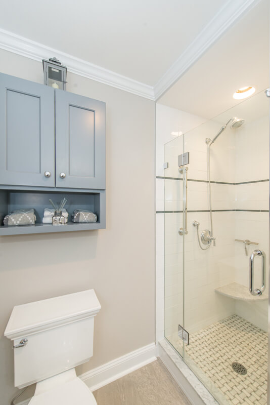 Grey and white hall bathroom remodel with Kohler accessories, grey shaker tank topper cabinet, frameless shower door with subway tile and accent stripe with niche, corner shelf and basketweave shower floor in Randolph, NJ renovated by JMC Home Improvement Specialists