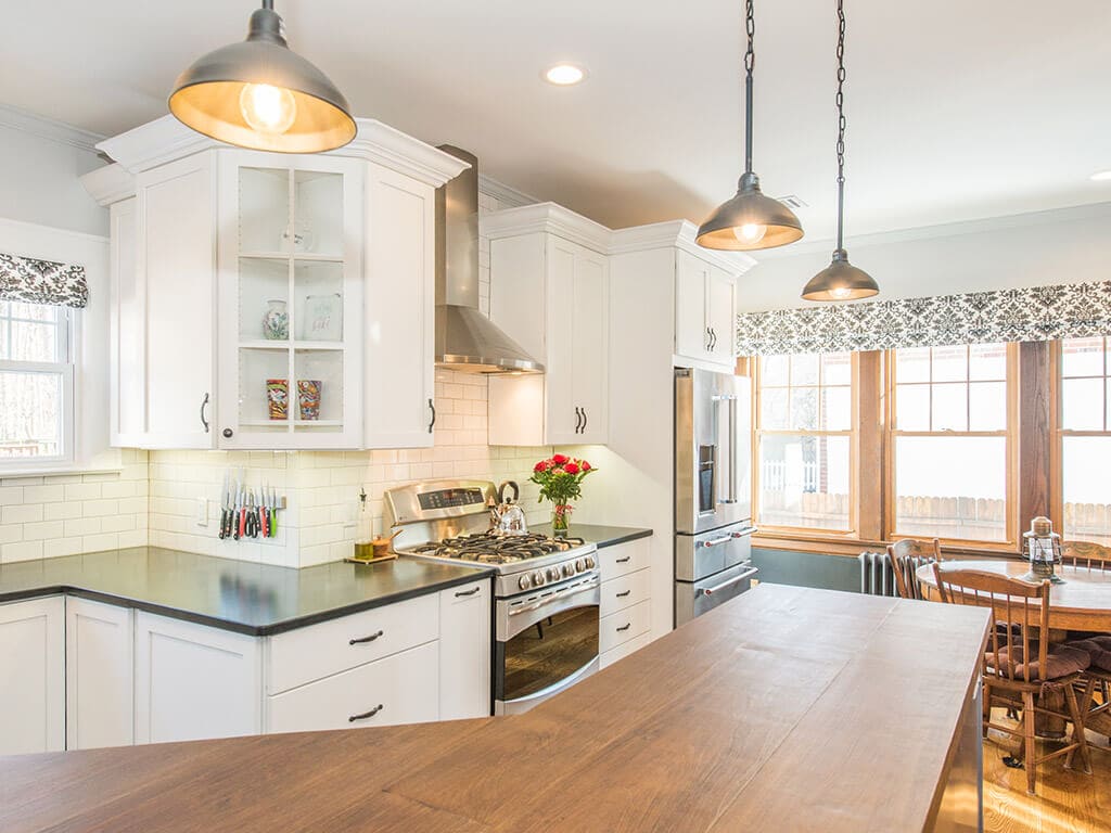 Open concept farmhouse two tone kitchen remodel with hardwood flooring, white shaker cabinets, crown molding, subway tile backsplash, concrete countertop on grey island with pendants and highhats, free standing hood and stainless steel appliances in Morristown, NJ renovated by JMC Home Improvement Specialists