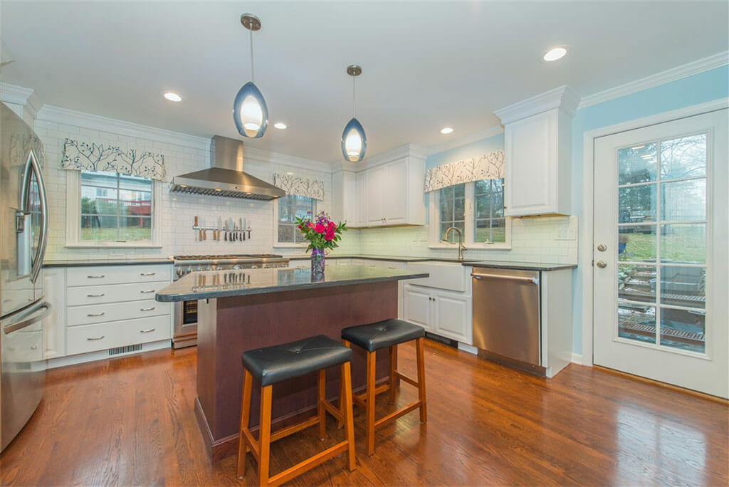 White kitchen remodel with hardwood flooring, white shaker cabinets, crown molding, cherry island with granite counters, subway tile backsplash, freestanding hood in Bernardsville, NJ renovated by JMC Home Improvement Specialists