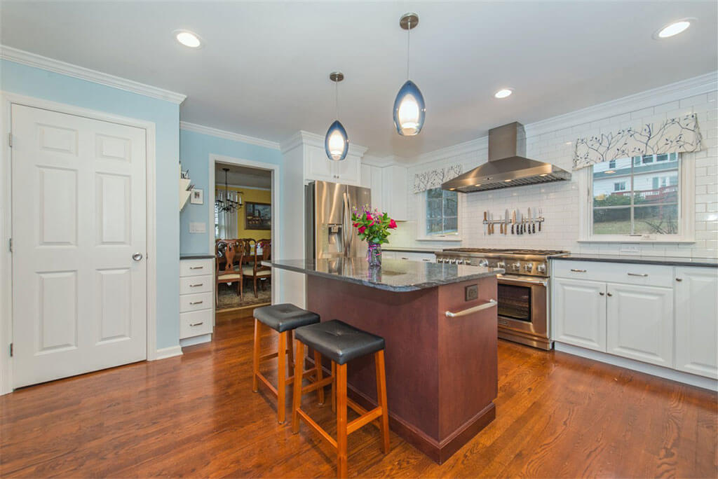 Two tone kitchen remodel with hardwood flooring, white shaker cabinets, crown molding, cherry island with granite counters, pendant lighting above island and LED highhats, subway tile backsplash, freestanding hood in Bernardsville, NJ renovated by JMC Home Improvement Specialists