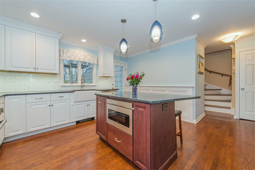 Two tone kitchen remodel with hardwood flooring, white shaker cabinets, crown molding, cherry island with granite counters, built in microwave, pendant lighting and LED highhats, subway tile backsplash, freestanding hood in Bernardsville, NJ renovated by JMC Home Improvement Specialists