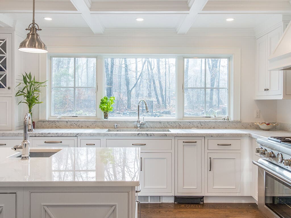 Award winning cape cod white kitchen remodel with white inset shaker cabinets, nano glass counter at island, 2” thick carerra marble counters, triple large windows above sink, two sinks with 7” oak hardwood flooring in Boonton, NJ renovated by JMC Home Improvement Specialists
