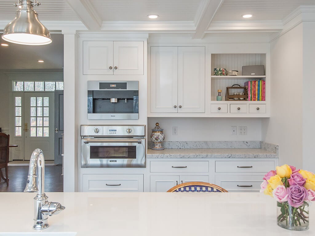 Cape cod white kitchen remodel with white inset shaker cabinets, nano glass counter at island with sink, 2” thick carerra marble counters, built in coffee machine, open shelving with wainscot  panels to match ceiling panels in Boonton, NJ renovated by JMC Home Improvement Specialists