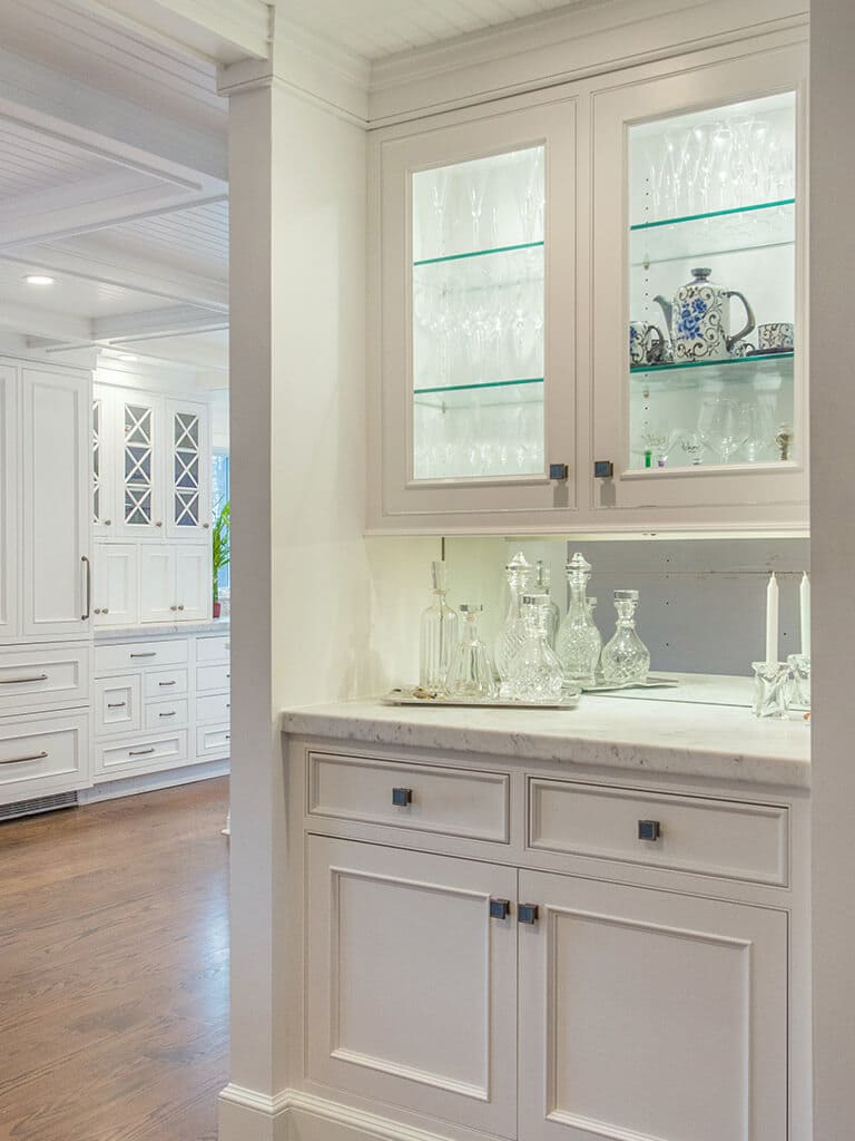 Award winning open concept cape cod kitchen with bar area with glass cabinets and lighting, white inset shaker cabinets with marble counter, crown molding, coffered ceiling and 7” oak flooring throughout in Boonton, NJ renovated by JMC Home Improvement Specialists