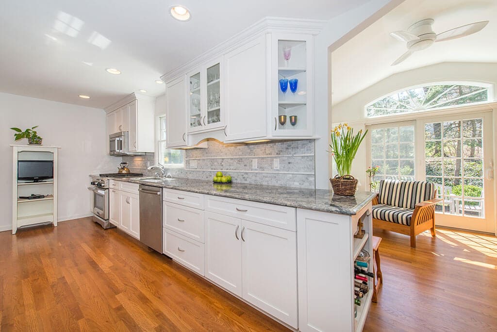 Open concept white kitchen remodel with white shaker cabinets, glass upper cabinet, granite countertops, vaulted ceilings in sunroom with transom windows and French doors and hardwood flooring in Chatham, NJ renovated by JMC Home Improvement Specialists