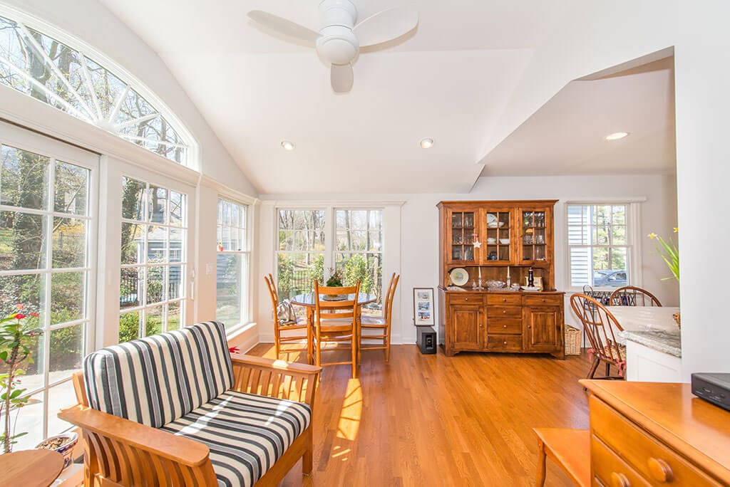 White sunroom with vaulted ceilings, ceiling fan, highhats, hardwood flooring and transom arch window over French doors in Chatham, NJ renovated by JMC Home Improvement Specialists