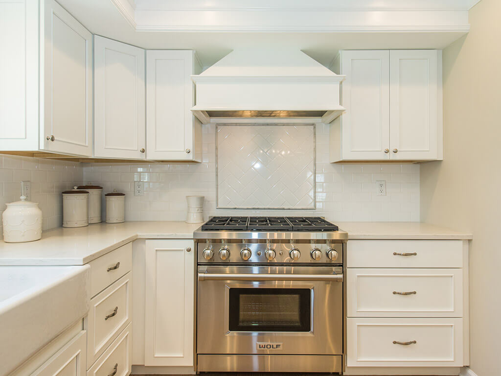 White kitchen remodel with shaker cabinets, quartz countertops, subway tile backsplash, custom wood hood, crown molding, apron sink and hardwood flooring in Morris County, NJ renovated by JMC Home Improvement Specialists