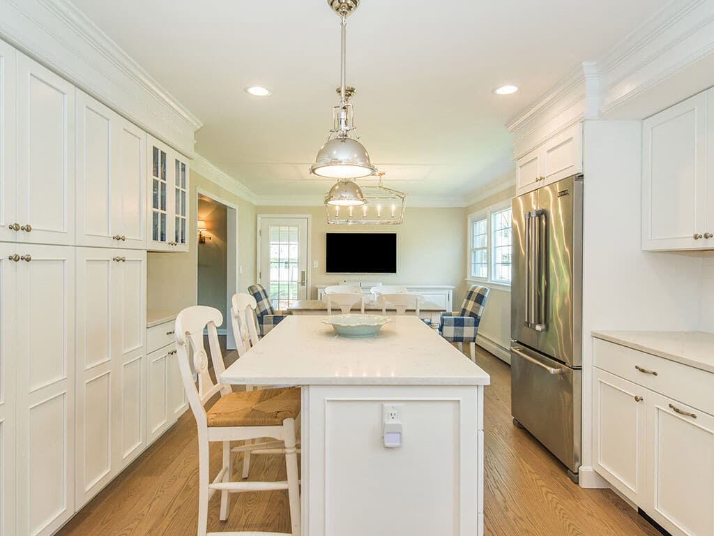 Open concept white kitchen remodel with cabinets, quartz countertops, subway tile backsplash, crown molding, apron sink, stainless appliances and hardwood flooring in Morris County, NJ renovated by JMC Home Improvement Specialists