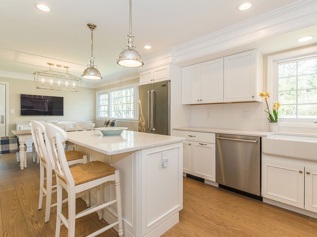 White kitchen remodel with cabinets, quartz countertops, subway tile backsplash, crown molding, apron sink, stainless appliances, wood hood and hardwood flooring in Morristown, NJ renovated by JMC Home Improvement Specialists