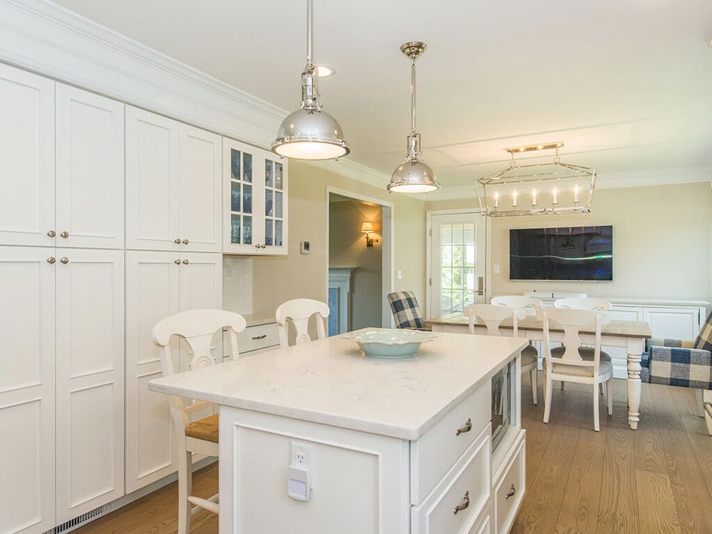 Open concept white kitchen remodel with white cabinets,  quartz countertops, crown molding, pendant lighting over island, wall removed for dining area and hardwood flooring in Morristown, NJ renovated by JMC Home Improvement Specialists