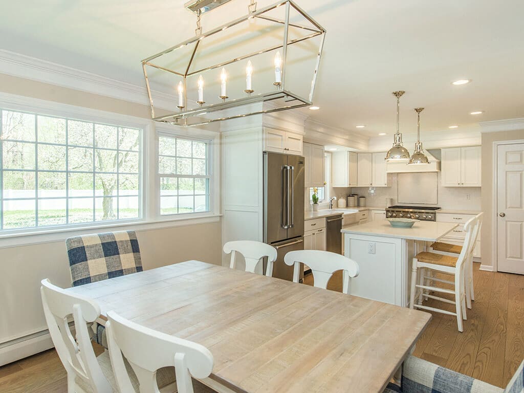 Open concept white kitchen remodel with white cabinets, quartz countertops, crown molding, pendant lighting over island, stainless appliances, wood hood and hardwood flooring in Morristown, NJ renovated by JMC Home Improvement Specialists