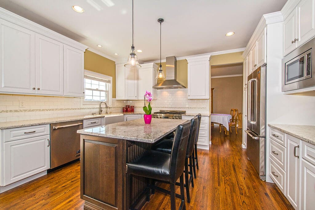 Two tone open concept kitchen remodel with cherry island and white cabinets, granite counters, pendants over island, subway tile backsplash with mosaic strip in Rockaway, NJ renovated by JMC Home Improvement Specialists
