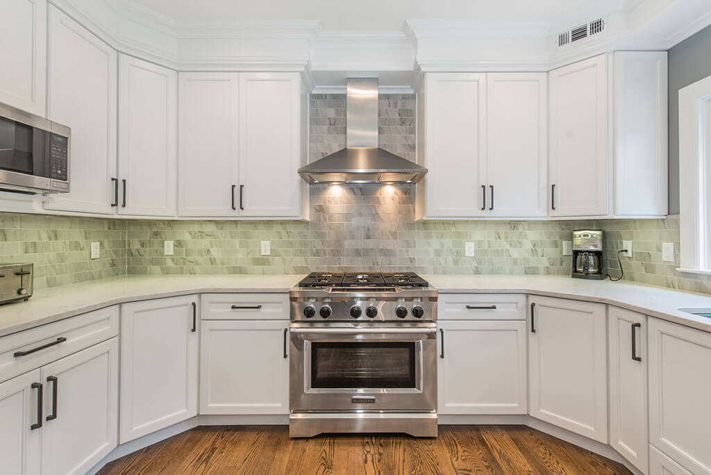 White  kitchen remodel with shaker cabinets with crown molding, quartz counters, peninsula, freestanding stainless hood and marble backsplash in Florham Park, NJ renovated by JMC Home Improvement Specialists