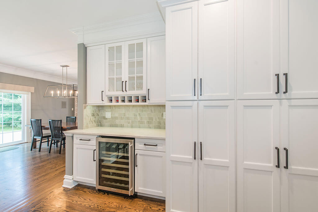 White open floor plan kitchen remodel with shaker pantry cabinets, glass cabinet doors, wine fridge, quartz counters, and marble backsplash in Florham Park, NJ renovated by JMC Home Improvement Specialists