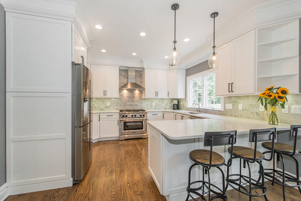 White open concept kitchen remodel with shaker cabinets, open shelving, quartz counters, pendant lighting over peninsula, freestanding metal hood and subway tile marble backsplash in Florham Park, NJ renovated by JMC Home Improvement Specialists