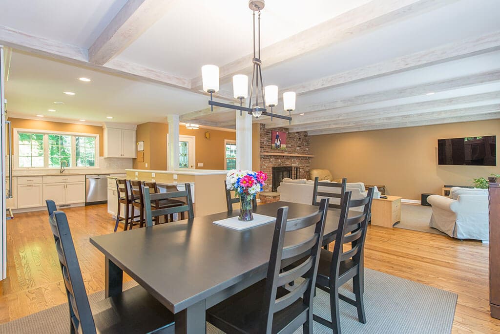 Open floor plan kitchen remodel with dining area, exposed wood beams in ceiling and hardwood flooring throughout in Mendham, NJ renovated by JMC Home Improvement Specialists