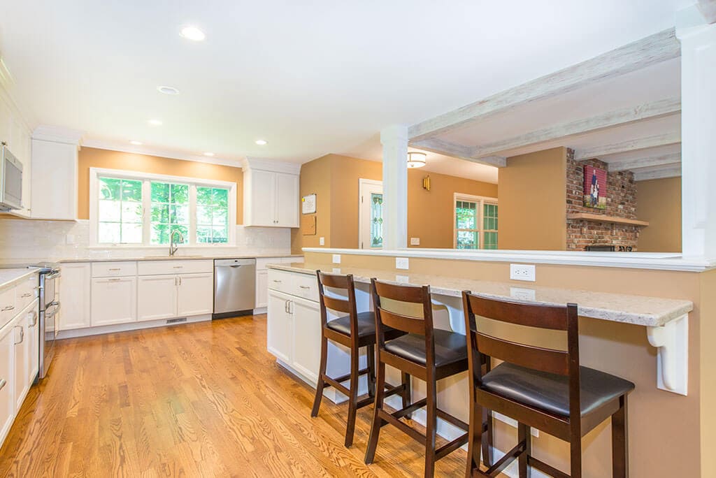 Open floor plan white kitchen remodel with shaker cabinets, quartz counters, exposed wood beams in ceiling and hardwood flooring throughout in Mendham, NJ renovated by JMC Home Improvement Specialists