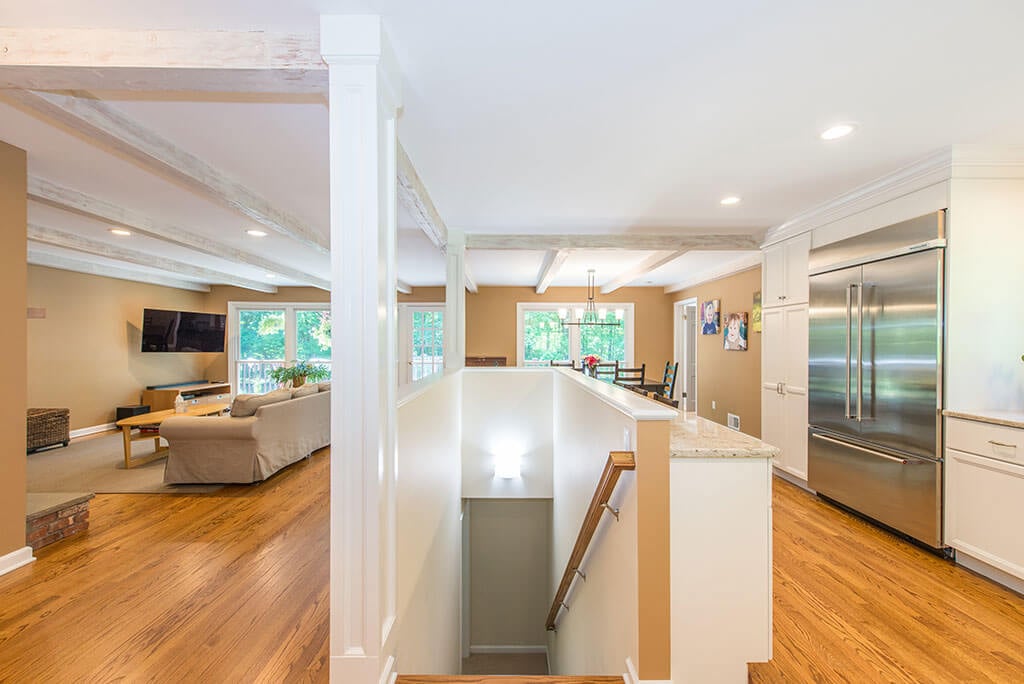 Open floor plan white kitchen remodel with shaker cabinets, quartz counters, stainless appliances, wood beams, stairs to basement and hardwood flooring throughout in Mendham, NJ renovated by JMC Home Improvement Specialists