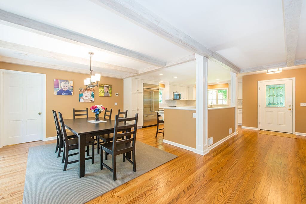 Open floor plan remodel with entrance to home, wood beams, exposed stairs to basement, dining area and hardwood flooring throughout in Mendham, NJ renovated by JMC Home Improvement Specialists
