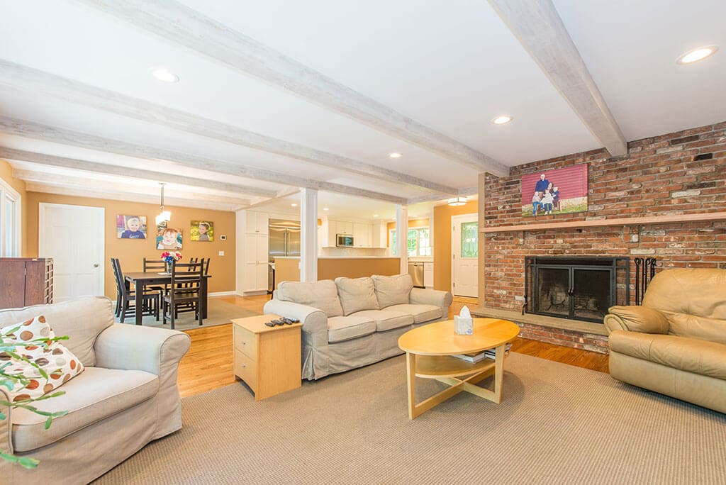 Open floor plan remodel with brick fireplace in family room, wood beams, exposed stairs to basement, dining area and kitchen remodel with hardwood flooring throughout in Mendham, NJ renovated by JMC Home Improvement Specialists