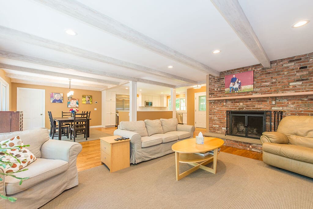 Open floor plan remodel with brick fireplace in family room, wood beams, exposed stairs to basement, dining area and kitchen remodel with hardwood flooring throughout in Mendham, NJ renovated by JMC Home Improvement Specialists