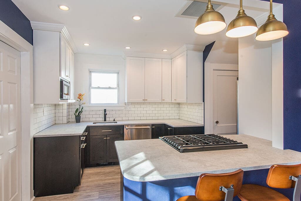 Black and white kitchen remodel with white upper cabinets, black lower cabinets, white subway tile backsplash,  seating at peninsula with quartz counters, wall removed with exposed beam in Montclair, NJ renovated by JMC Home Improvement Specialists