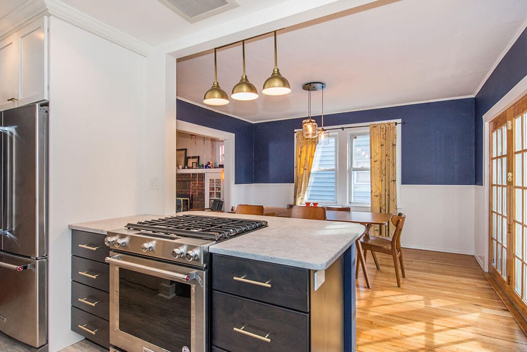 Open concept black and white kitchen remodel with white upper cabinets, black lower cabinets, white subway tile backsplash,  seating at peninsula with quartz counters, wall removed with exposed beam in Montclair, NJ renovated by JMC Home Improvement Specialists