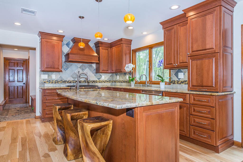 Kitchen remodel with mud room to open concept kitchen with freestanding wood hood, granite counters, crown molding, pendants over island, pot filler with mosaic backsplash, undermount sink and bar sink in Morristown, NJ remodeled by JMC Home Improvement Specialists