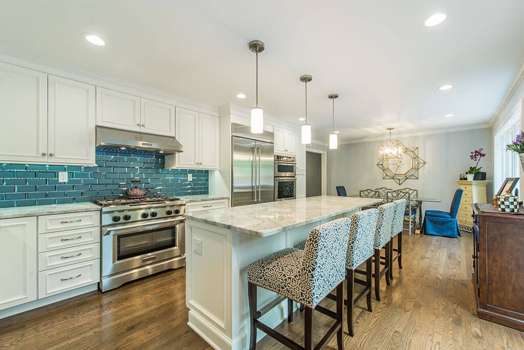 Open floor plan white kitchen with bevel edge glass tile backsplash, extended kitchen island for seating, granite counters, hardwood floor throughout in Morristown, NJ renovated by JMC Home Improvement Specialists