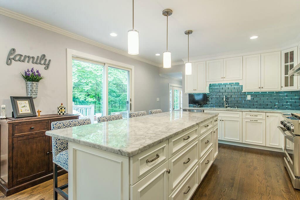 White eat-in kitchen remodel with beveled edge glass tile backsplash, granite counters, pendant lights above island and LED highhats, sliding door to deck, hardwood flooring in Morristown, NJ renovated by JMC Home Improvement Specialists