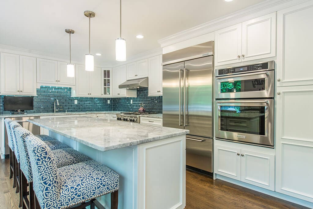 Kitchen remodel with white kitchen cabinets, with beveled edge glass tile backsplash, granite counters, pendant lights above island and LED highhats, metal hood, double oven in Morristown, New Jersey renovated by JMC Home Improvement Specialists