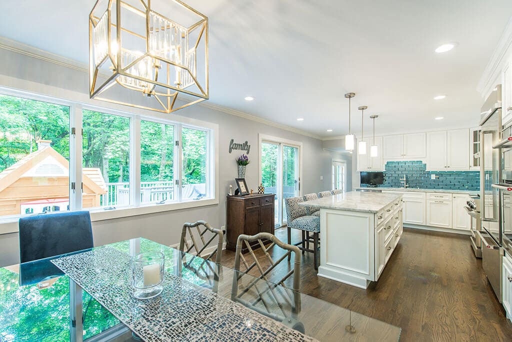 Open concept kitchen remodel with white kitchen cabinets, with beveled edge glass tile backsplash, granite counters, pendant lights above island and LED highhats, dining area, hardwood flooring with sliding door to deck in Morris County, New Jersey renovated by JMC Home Improvement Specialists