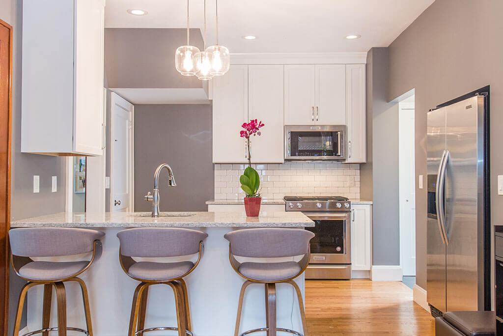 Small white contemporary kitchen remodel with subway tile backsplash, in wall refrigerator, granite counters with pendant and LED highhat lights in Maplewood, NJ remodeled by JMC Home Improvement Specialists