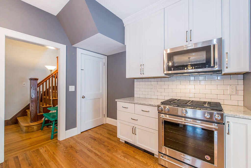 Small white contemporary kitchen remodel with subway tile backsplash, granite counters, 42” tall cabinets microwave over stove with hardwood flooring in Maplewood, NJ remodeled by JMC Home Improvement Specialists