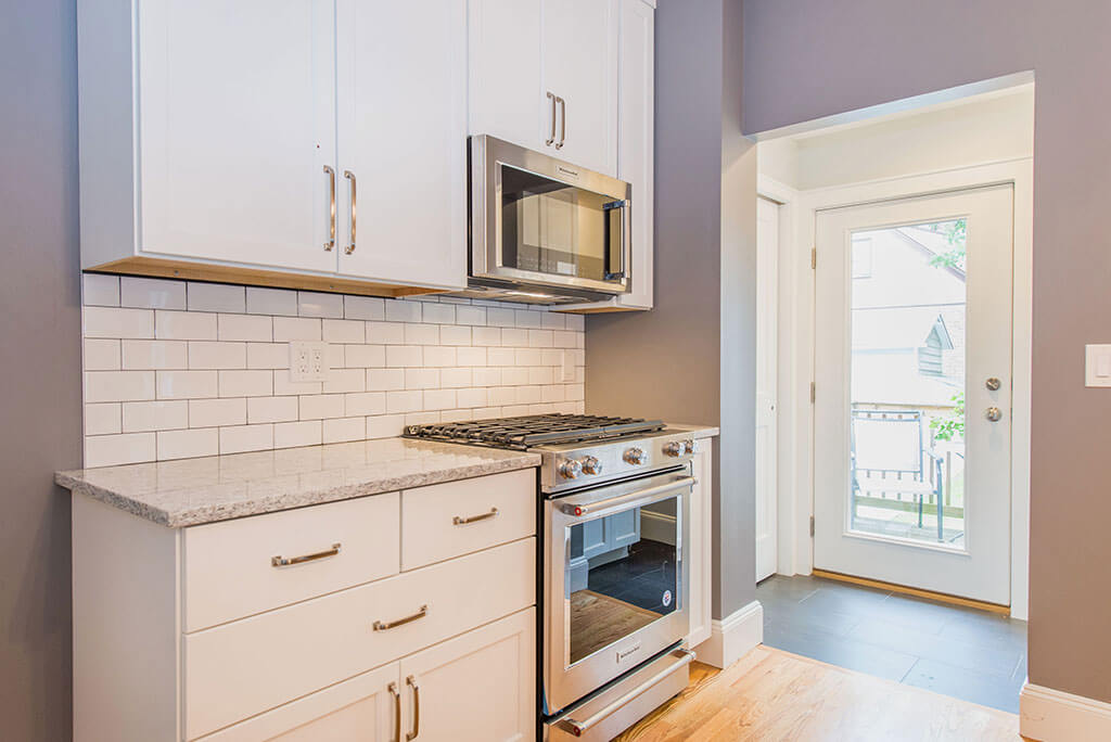 Small white contemporary kitchen remodel with subway tile backsplash, granite counters, 42” tall cabinets microwave over stove with hardwood flooring in Essex, NJ remodeled by JMC Home Improvement Specialists