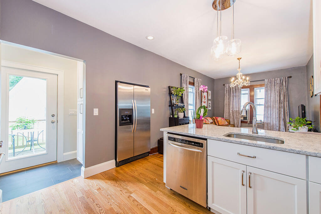 Small white contemporary open concept kitchen remodel with granite countertop, pendant lighting above peninsula, in wall refrigerator with hardwood flooring in Essex, NJ remodeled by JMC Home Improvement Specialists