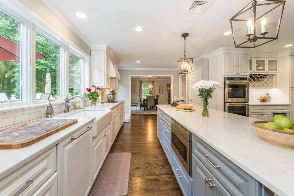 Two tone kitchen remodel with grey island, microwave drawer, white apron sink with triple windows above, hidden dishwasher with panel, in Denville, NJ remodeled by JMC Home Improvement Specialists