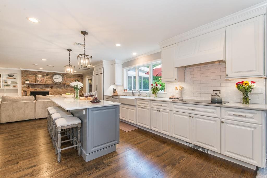 Open concept Grey and white kitchen remodel with grey island with quartz counter, white apron sink, wood hood over cooktop, undercabinet lighting, subway tile backsplash, exposed brick in family room in Denville, NJ remodeled by JMC Home Improvement Specialists