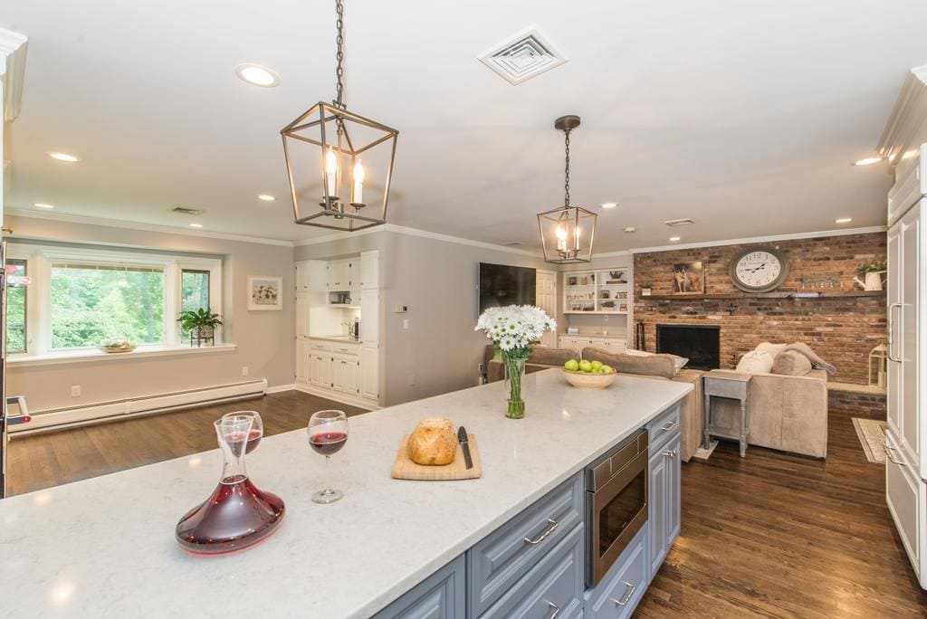 Open concept grey and white kitchen remodel with grey island with quartz counter and microwave shelf, paneled fridge, exposed brick in family room in Denville, NJ remodeled by JMC Home Improvement Specialists