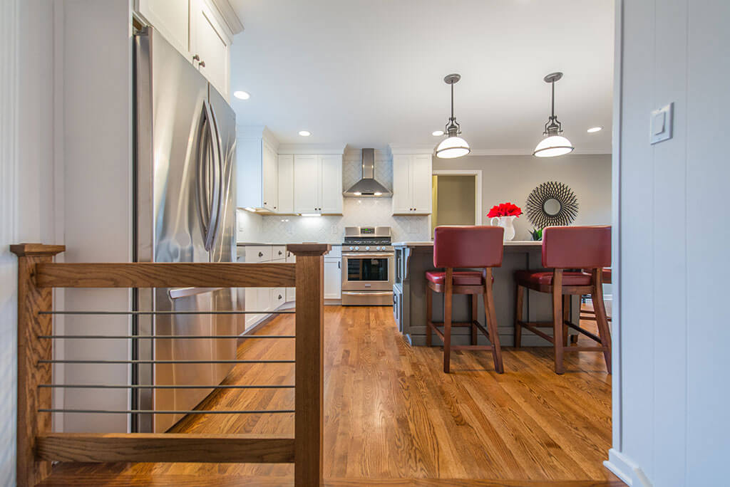 Eat in two tone open concept kitchen remodel with hardwood flooring, white shaker cabinets, quartz counters, pendant lighting over island, metal railing, freestanding hood and LED highhats in Parsippany, NJ remodeled by JMC Home Improvement Specialists