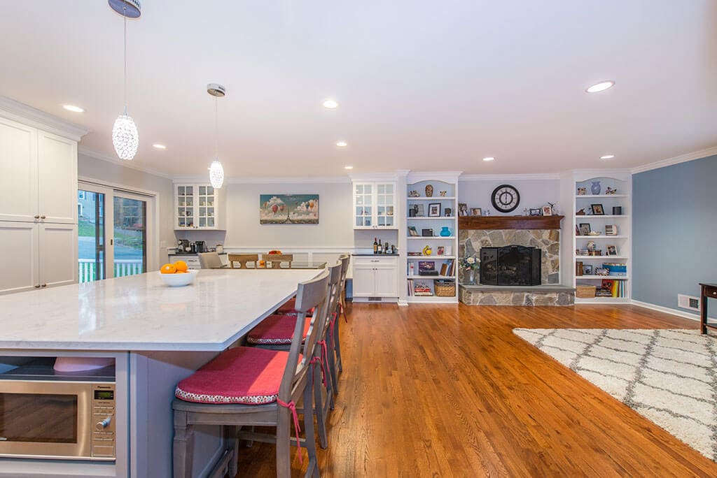 Open concept kitchen with flush header, hardwood flooring, bookshelves, stone fireplace, microwave shelf in eat in island with pendant lighting in Randolph, NJ remodeled by JMC Home Improvement Specialists