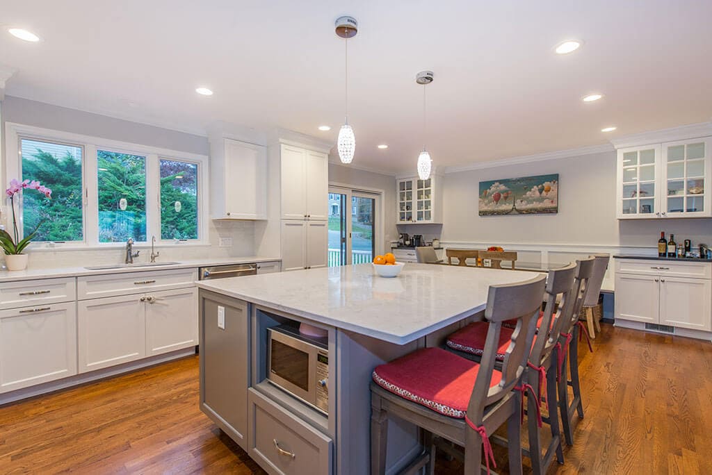 White kitchen remodel with hardwood flooring, triple window above sink, microwave shelf in eat in grey island with pendant lighting in Randolph, NJ remodeled by JMC Home Improvement Specialists