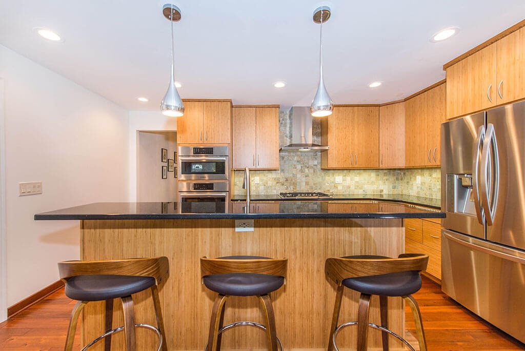 Modern bamboo eat-in kitchen remodel with slab doors, with granite countertops, pendant and high hat lighting with free standing hood over cooktop with wall ovens Randolph, NJ renovated by JMC Home Improvement Specialists