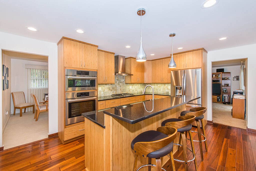 Modern bamboo eat-in kitchen remodel with slab doors, with granite countertops, pendant and high hat lighting with free standing hood over cooktop with wall ovens Morris County, NJ renovated by JMC Home Improvement Specialists