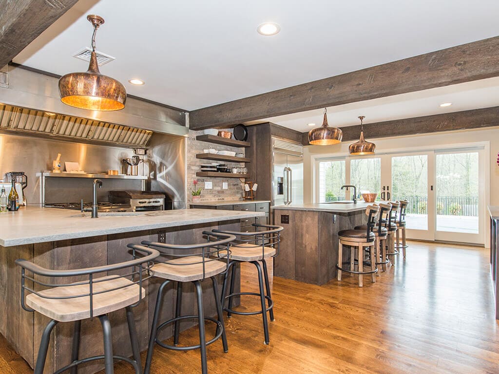 Rustic open floor plan kitchen with concrete island and peninsula, industrial  range and hood, wood beams and hardwood flooring throughout in Rockaway, NJ remodeled by JMC Home Improvement Specialists