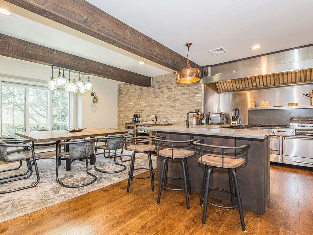 Rustic open floor plan kitchen with exposed brick, concrete peninsula, industrial  range and hood, wood beams and hardwood flooring throughout in Rockaway, NJ remodeled by JMC Home Improvement Specialists