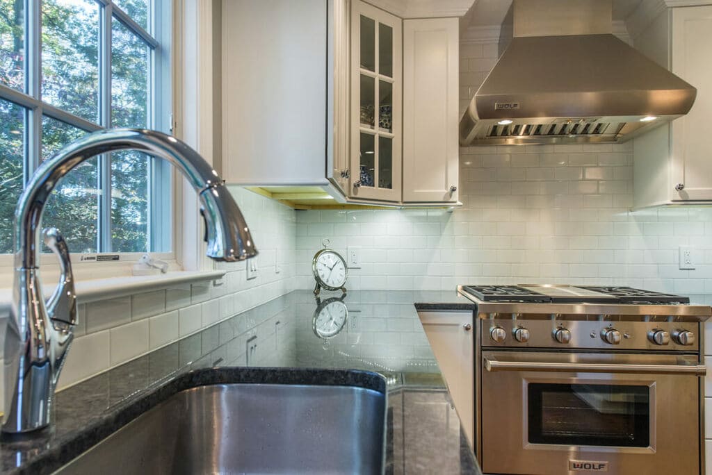 White kitchen with glass cabinet door, white subway tile backsplash, metal freestanding hood black with pearl granite countertop with undermount sink in Springfield, NJ remodeled by JMC Home Improvement Specialists