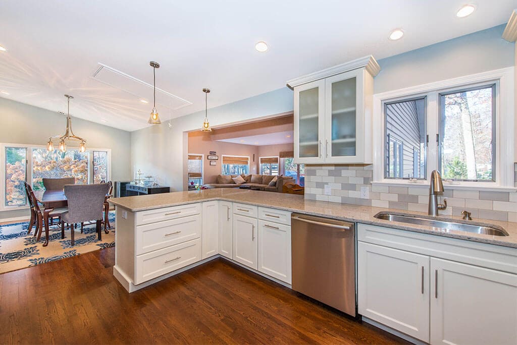 Wall removal for open floor concept kitchen with white Shaker cabinets and frosted glass cabinets with subway tile backsplash, pendant lighting and undermount stainless sink with hardwood floors in Summit, NJ remodeled by JMC Home Improvement Specialists